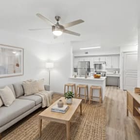A living room with a grey couch, a wooden table, and a ceiling fan.