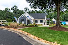 A house with a grey roof and a sign that says "Now Open" is surrounded by greenery.