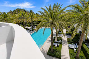 A pool surrounded by palm trees and a white building.