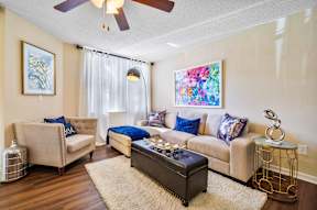 A living room with a beige couch, a chair, a coffee table, and a painting on the wall.