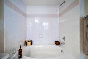 A white bathroom with a white tub and a bottle of wine.