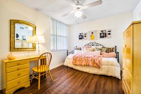 A bedroom with a bed, a desk, a chair, and a ceiling fan.