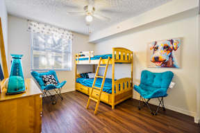 A room with a bunk bed, a chair, and a painting of a dog.