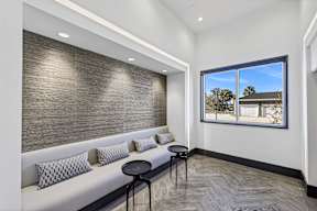 A room with a long white couch and a table with a black stool.