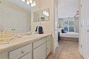 A bathroom with a vanity, mirror, and a bedroom in the background.
