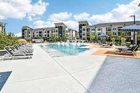 A pool area with sun loungers and a building in the background.