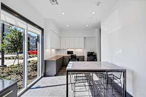 A modern kitchen with a table and chairs in the foreground and a red car visible through the glass door.