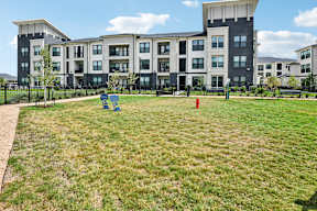 A large grassy area in front of apartment buildings with a red fire hydrant and a blue playground.