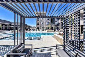 A pool area with a bench and a table under a pergola.