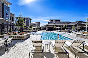 A sunny day at a poolside with chairs and a table.