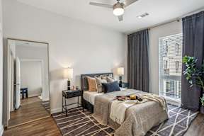 A bedroom with a large bed, a ceiling fan, and a view of a building outside the window.