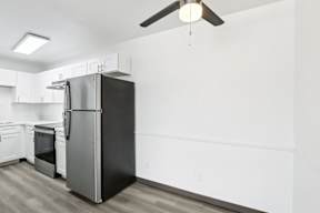 A black refrigerator in a kitchen with white walls and wooden flooring.