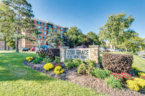 A sign for 2200 Grace Apartment Homes is surrounded by flowers and greenery.