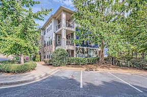A large two-story building with a balcony on the second floor is surrounded by trees and bushes.