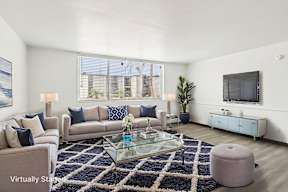 A living room with a glass coffee table and a large window.