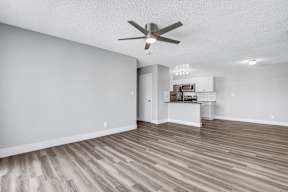 a living room with a ceiling fan and a kitchen in the background