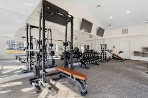 A gym with a variety of equipment including a squat rack, bench, and weights.