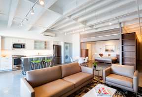 A modern living room with a brown leather couch and a kitchen area in the background.