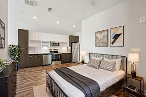A bedroom with a bed, nightstand, and a plant.