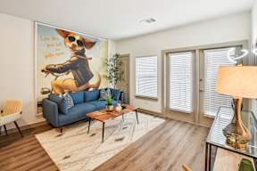 A living room with a blue couch and a poster of a dog on the wall.
