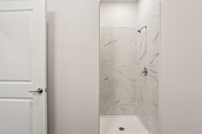 A white door is open to a bathroom with a marble shower.