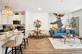 A modern kitchen with a bar area and a living room with a sofa and a painting of a dog.