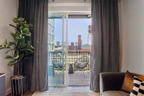 A living room with a grey couch and a view of a balcony with chairs.