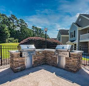 A stone wall with a grill on top and a pool in the background.