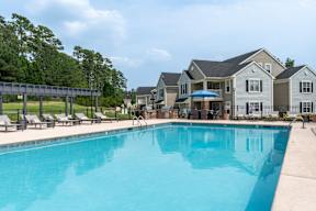 A large swimming pool in front of a building with a row of lounge chairs on the left.
