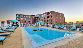 A swimming pool surrounded by lounge chairs and umbrellas in front of a brick building.