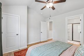 A bedroom with a bed, a ceiling fan, and a door.