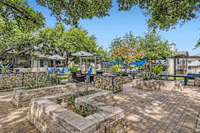 a patio with stone walls and trees and a fountain