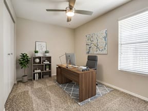 A room with a desk, chair, and a ceiling fan.