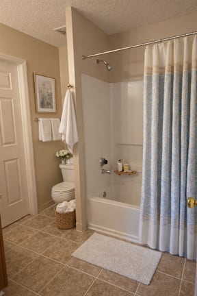 A bathroom with a toilet, a shower curtain, and a basket on the floor.