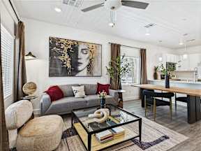 A modern living room with a grey couch, a glass coffee table, and a large abstract painting on the wall.