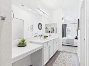 A white bathroom with a large mirror and a plant on the counter.