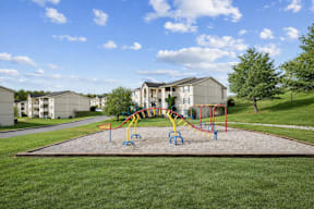 A playground with a slide and swings in front of apartment buildings.