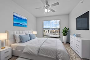 A bedroom with a large bed, a ceiling fan, and a painting on the wall.