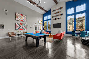 A pool table is surrounded by chairs in a room with wood flooring.