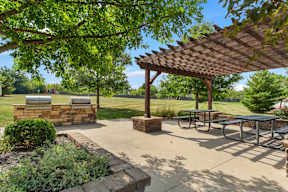 A picnic area with tables and a grill under a wooden pergola.