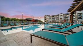 a swimming pool with blue chaise lounge chairs and a building in the background