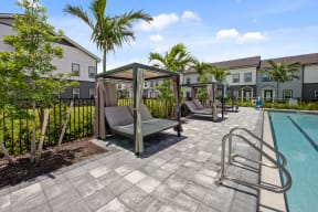 a pool with lounge chairs and hammocks and buildings in the background