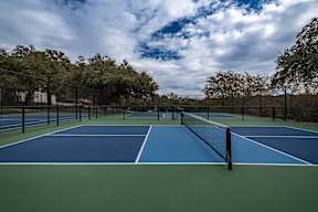 A tennis court surrounded by trees and a cloudy sky.