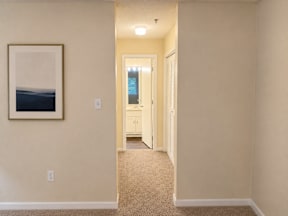 A hallway with a painting on the wall and a door at the end.