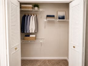 A white closet with clothes hanging and shelves with towels and a plant.
