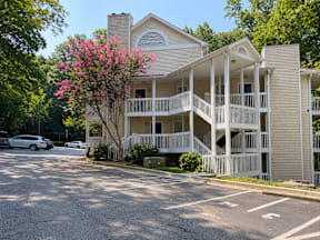 A two-story building with a balcony and a tree with pink flowers in front.