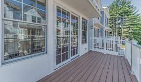 A wooden deck with a white railing and a view of a house across the street.
