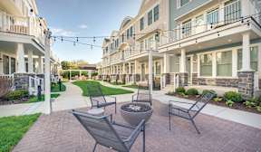 A patio with chairs and a fire pit in front of apartment buildings.