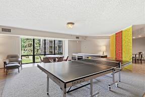 A ping pong table is in the middle of a room with a chair and a window.