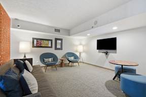 A living room with a grey couch, blue chairs, and a flat screen TV.